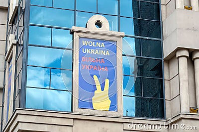 Blue and yellow poster with Wolna Ukraina text and a peace hand gesture city building window Editorial Stock Photo
